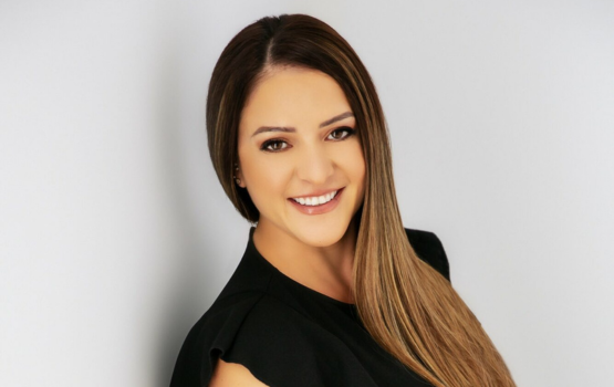 Woman with long straight highlighted hair wearing a black top against a white background